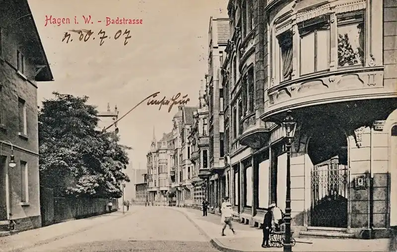 Straßenzug der Badstraße (1907) in Hagen, alte Fotografie in schwarz-weiß mit leichter Sepia-Tönung. Rechts eine Häuserreihe, links im Vordergrund ein Haus und einige Bäume hinter einer Mauer. Dahinter steht noch ein Haus, welches handschriftlich markiert wurde.